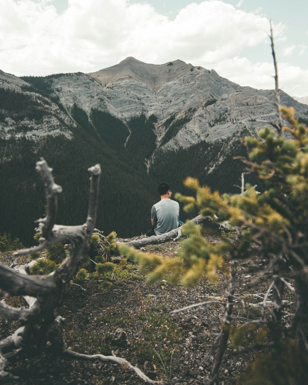 uomo seduto di fronte alla montagna che si affaccia all'indietro