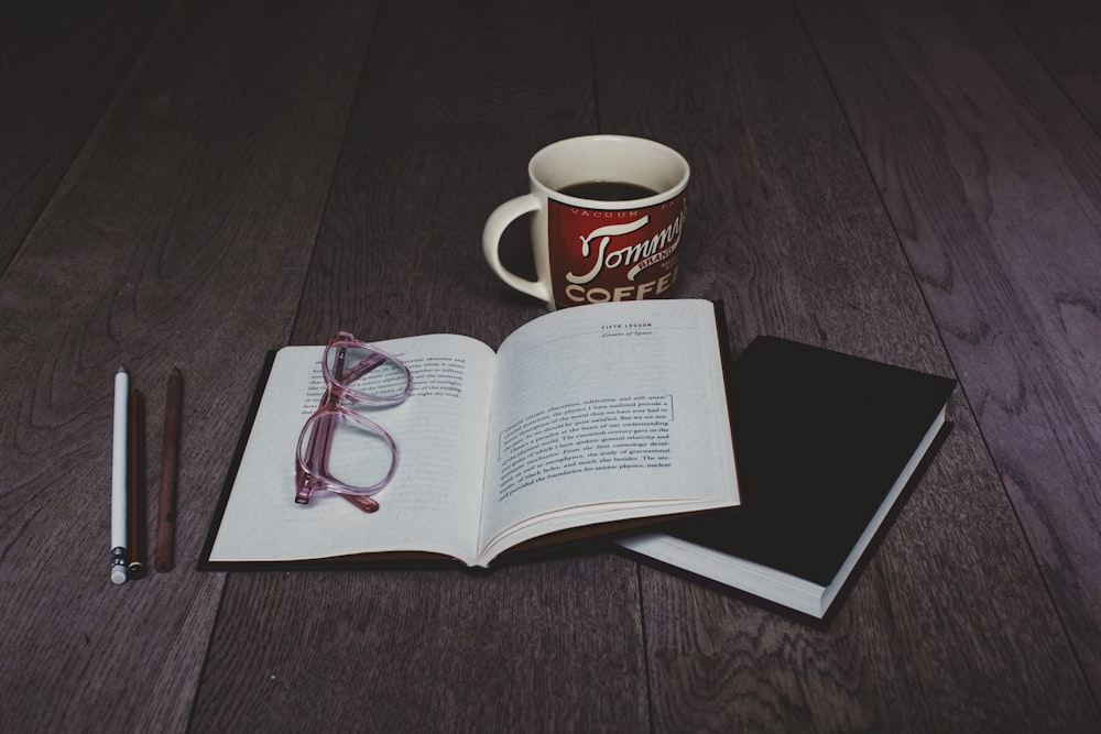 clear eyeglasses on top of white book page near white ceramic mug