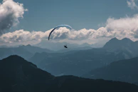 Paraglider soaring above the dramatic cirques, framed by ocean blue skies and verdant peaks.