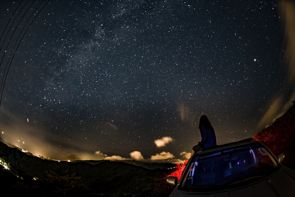 woman sitting on car while watching stars