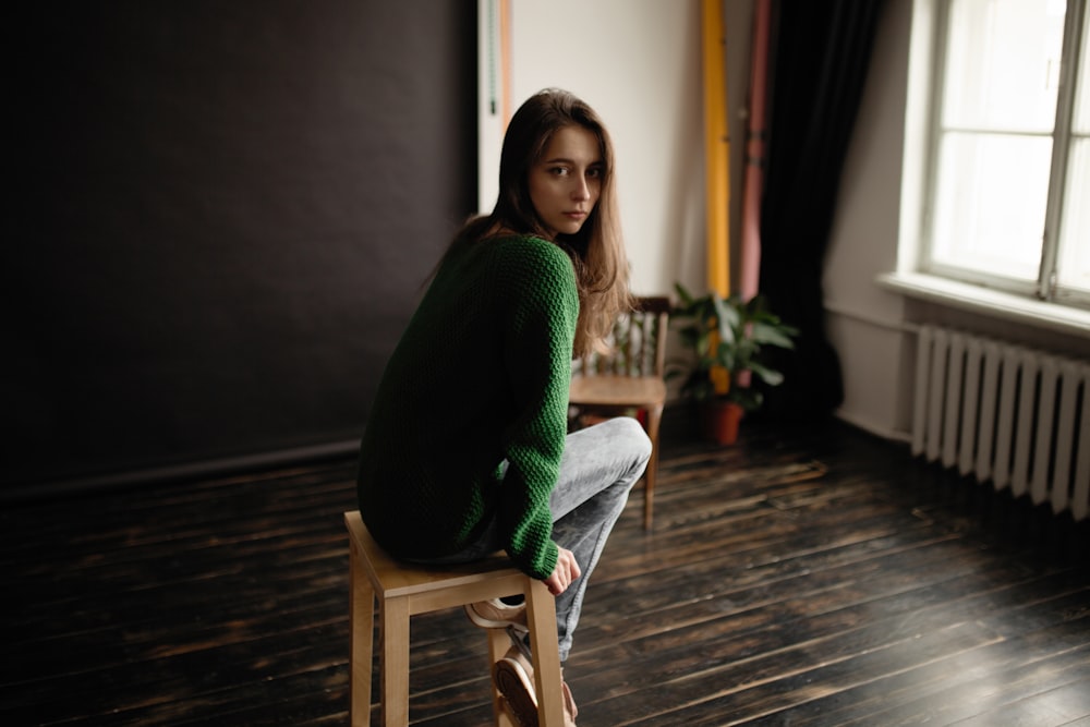woman wearing green sweater sitting on brown wooden stool