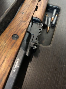 A close-up of a rugged rifle resting on a dark wooden table, highlighting its craftsmanship.