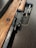 A wooden rifle with metallic components is placed on a dark wooden surface, accompanied by several bullets. The rifle showcases intricate metal parts with a visible bolt action mechanism.