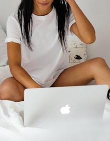 woman wearing white crew-neck t-shirt on bed holding silver MacBook