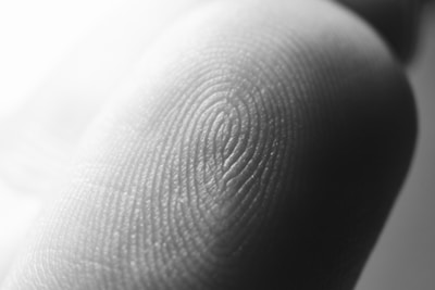 Close-up view of a finger with detailed emphasis on the skin texture and fingerprint pattern. The image highlights the intricate ridges and grooves forming unique loops and whorls.