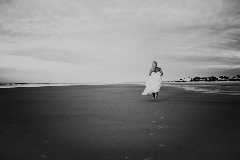 grayscale photo of woman walking on seashore