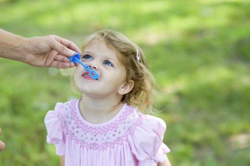 person hand holding bubble maker toy near toddler's mouth