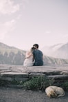 man and woman facing backward while woman's head on man's shoulder on tip of hill