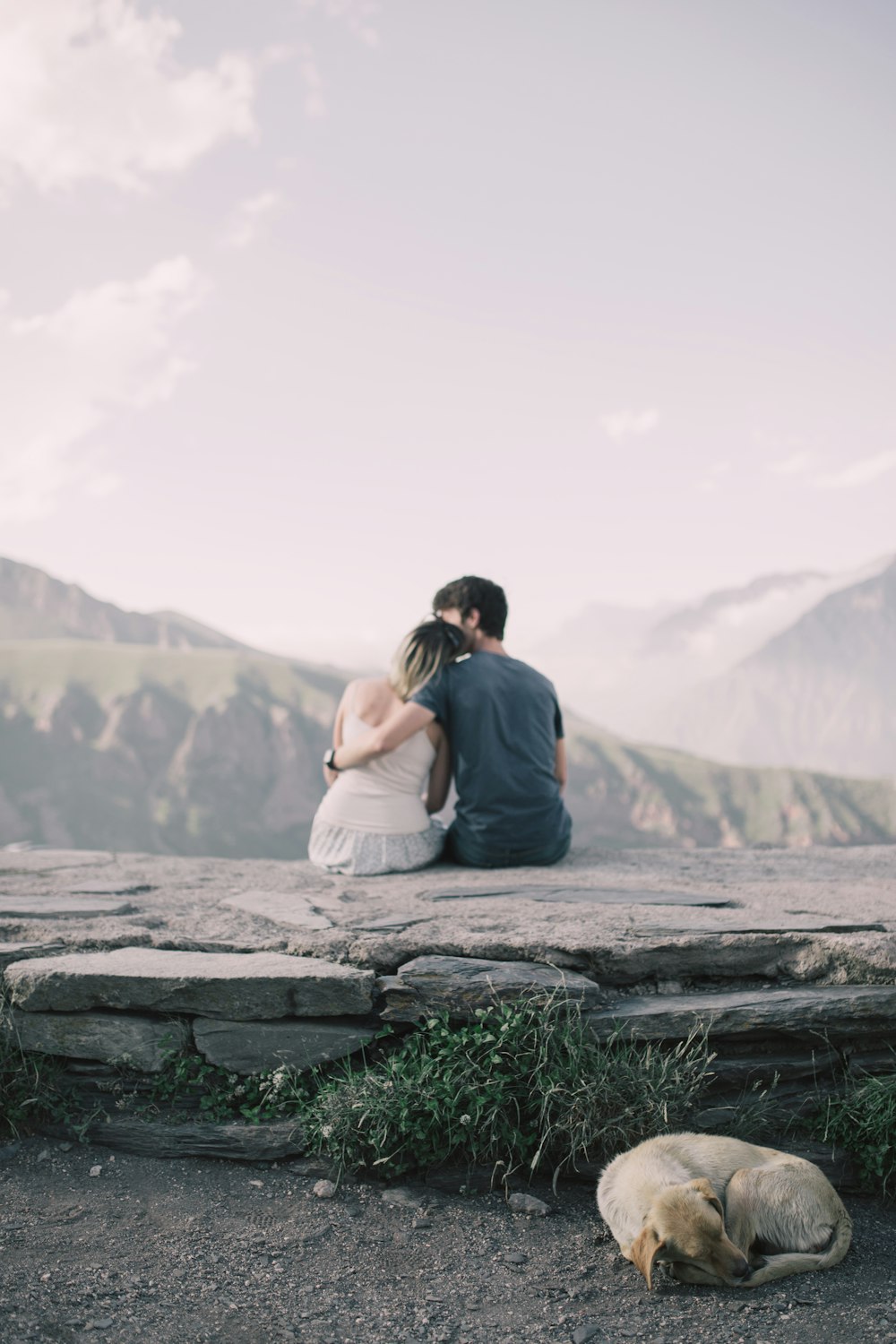 man and woman facing backward while woman's head on man's shoulder on tip of hill