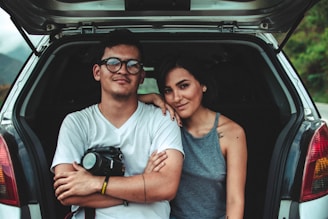 A young couple happily signing paperwork for their first car purchase at a modern dealership.