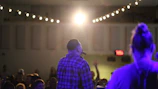 A close-up of hands holding a microphone in a dimly lit community center.