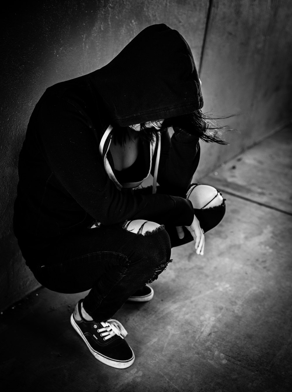 a woman sits alone against a wall holding her head