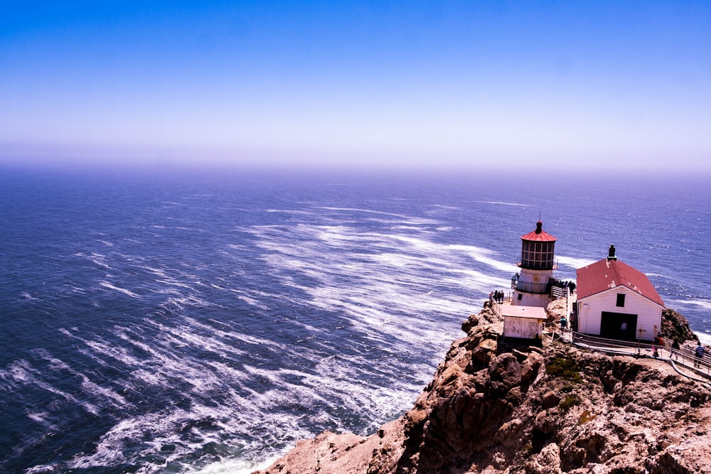 galpão branco e vermelho ao lado do farol na colina com vista para o mar