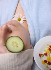 woman wearing blue robe lying with cucumber on eye