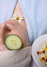 woman wearing blue robe lying with cucumber on eye