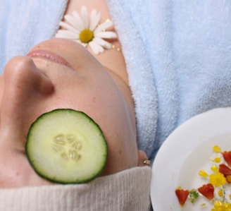 woman wearing blue robe lying with cucumber on eye