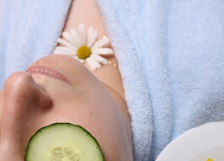 woman wearing blue robe lying with cucumber on eye