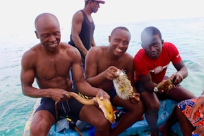 A group of smiling fishermen on a boat celebrating a big catch with fishing rods and gear visible.