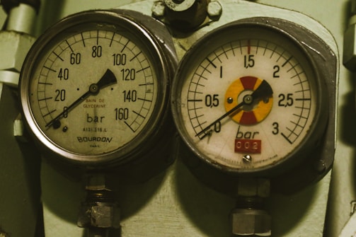 Two analog pressure gauges mounted on a metal surface, each displaying pressure measurements in bars. The left gauge has a range up to 160 bars, labeled with 'Bourdon' and 'Bain de Glycérine', while the right gauge goes up to 3 bars and includes a colored section on the dial.