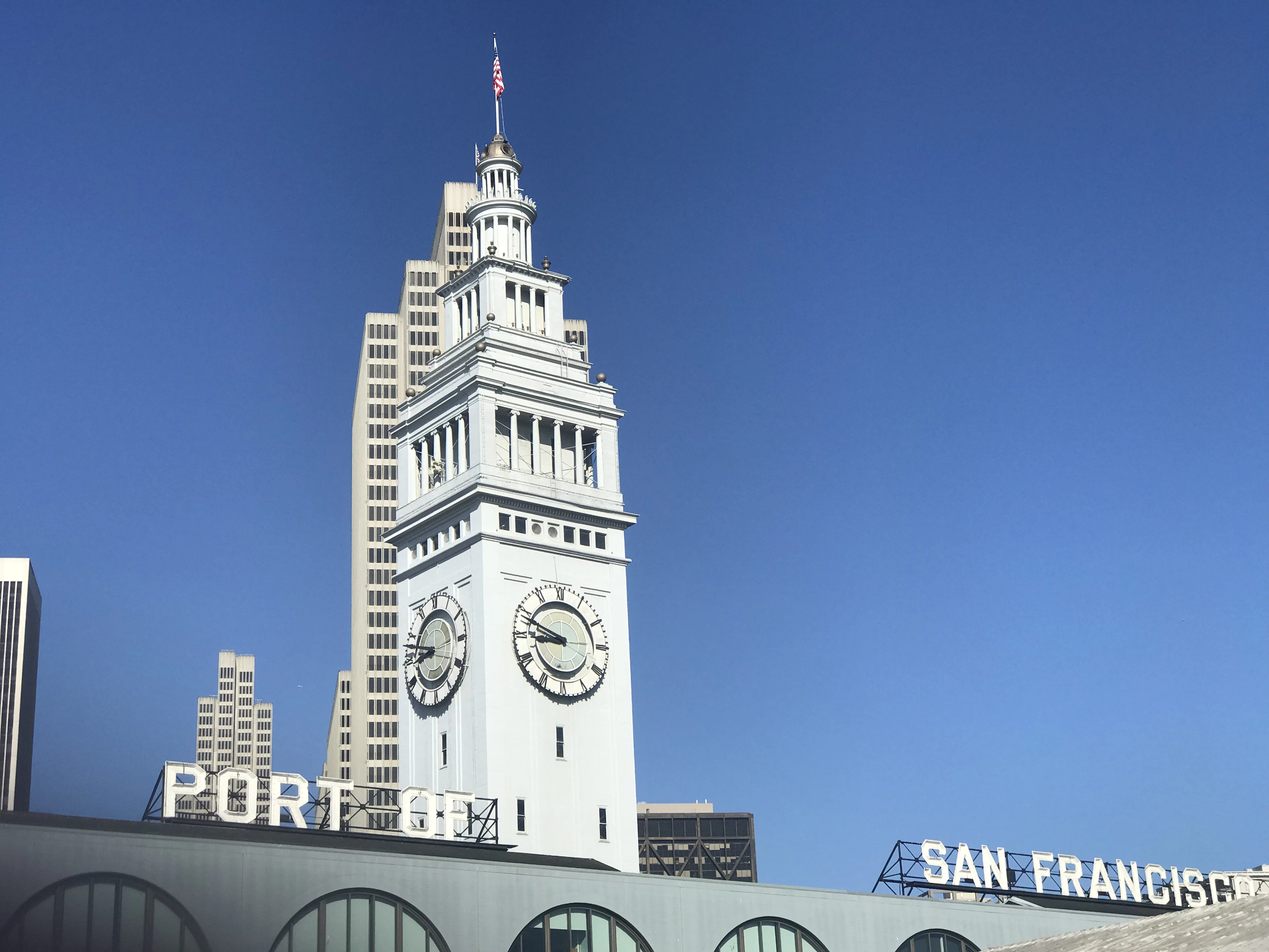 The clock tower of San Francisco's Ferry Building above signage reading "Port of San Francisco" against a clear blue sky