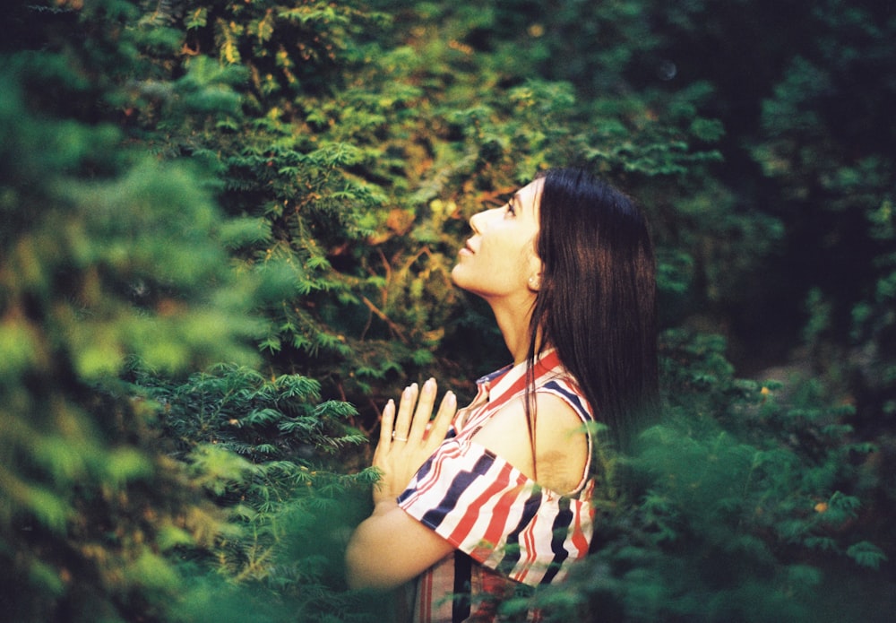 woman wearing white, red, and black striped cold-shoulder blouse surrounded by green leaf plants