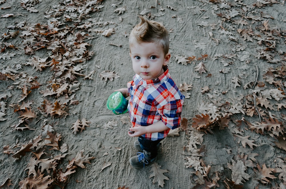 boy in white, blue, and orange plaid button-up shirt holding green cup