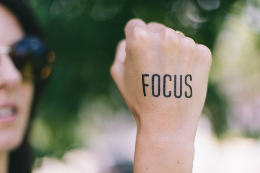 A woman (out of focus) holds up her fist, on which is tattooed the word 'focus'.