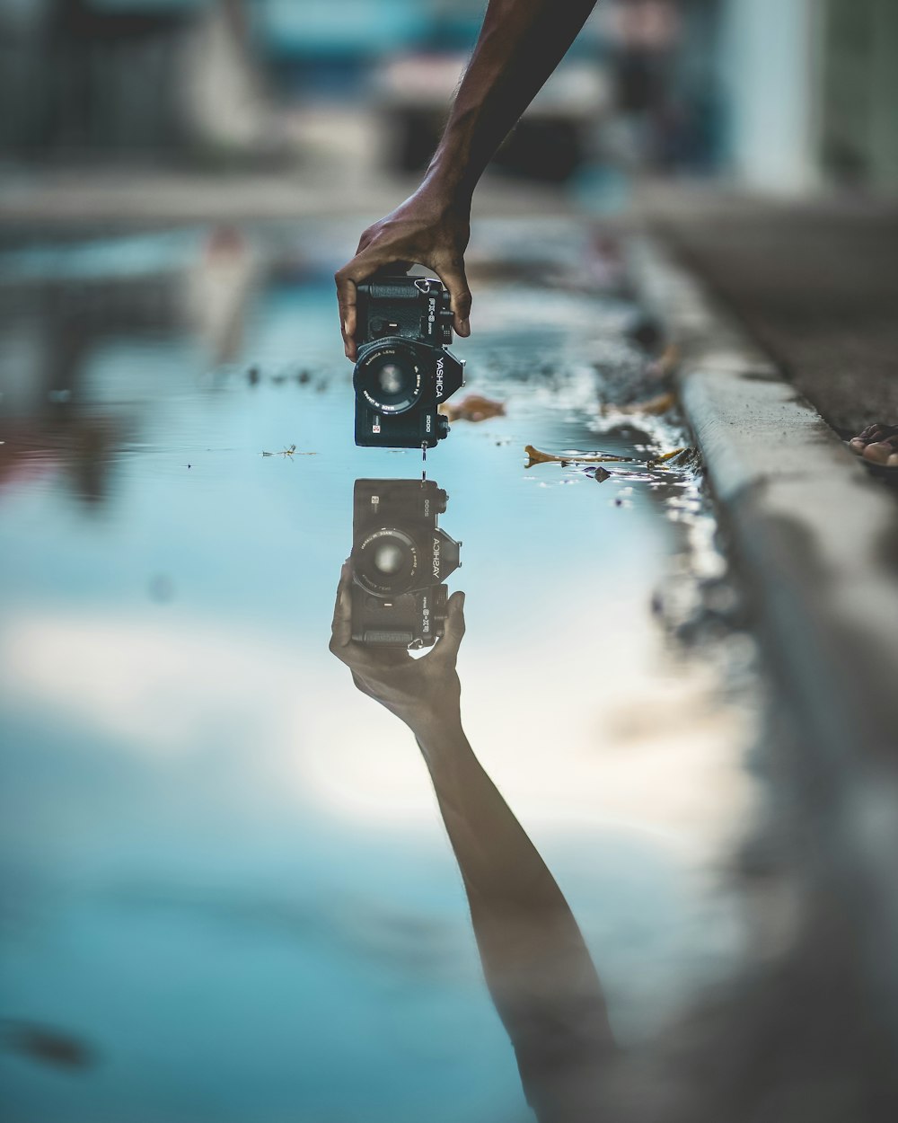 fotografia do espelho da pessoa segurando a câmera DSLR com reflexão da água