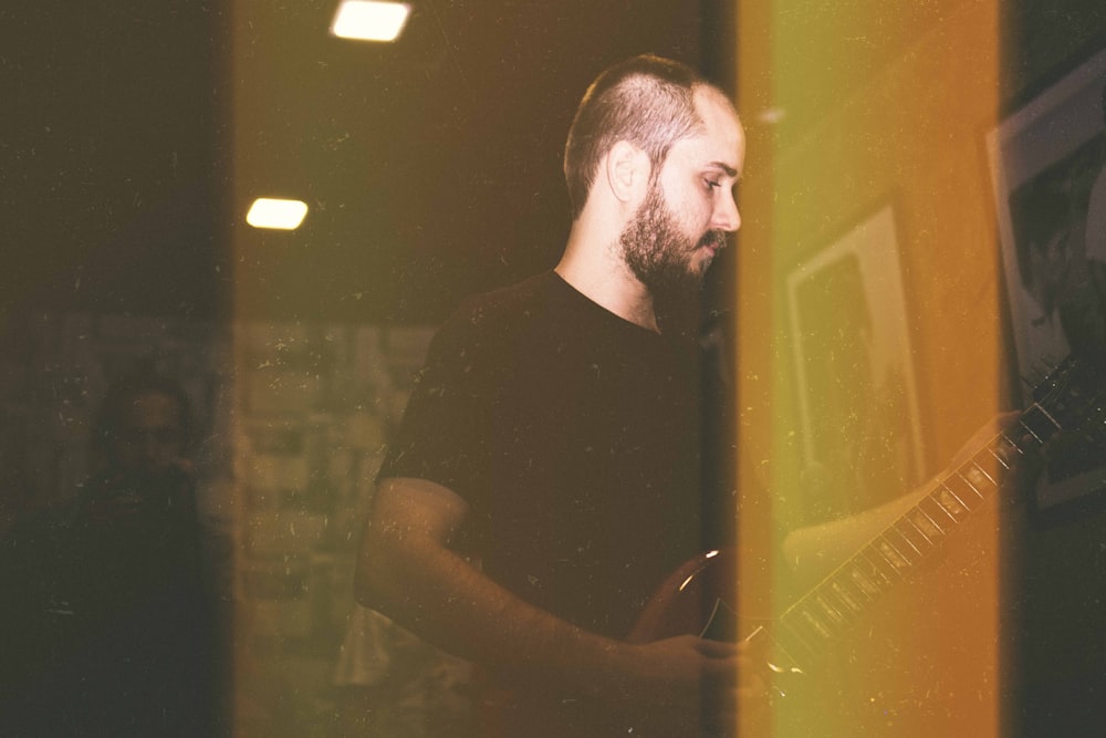 man wearing black crew-neck T-shirt playing red and black electric guitar