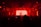 A dimly lit club scene with a DJ silhouetted against a bright red backdrop. The room is filled with people enjoying the atmosphere, and various speakers and lights are visible.