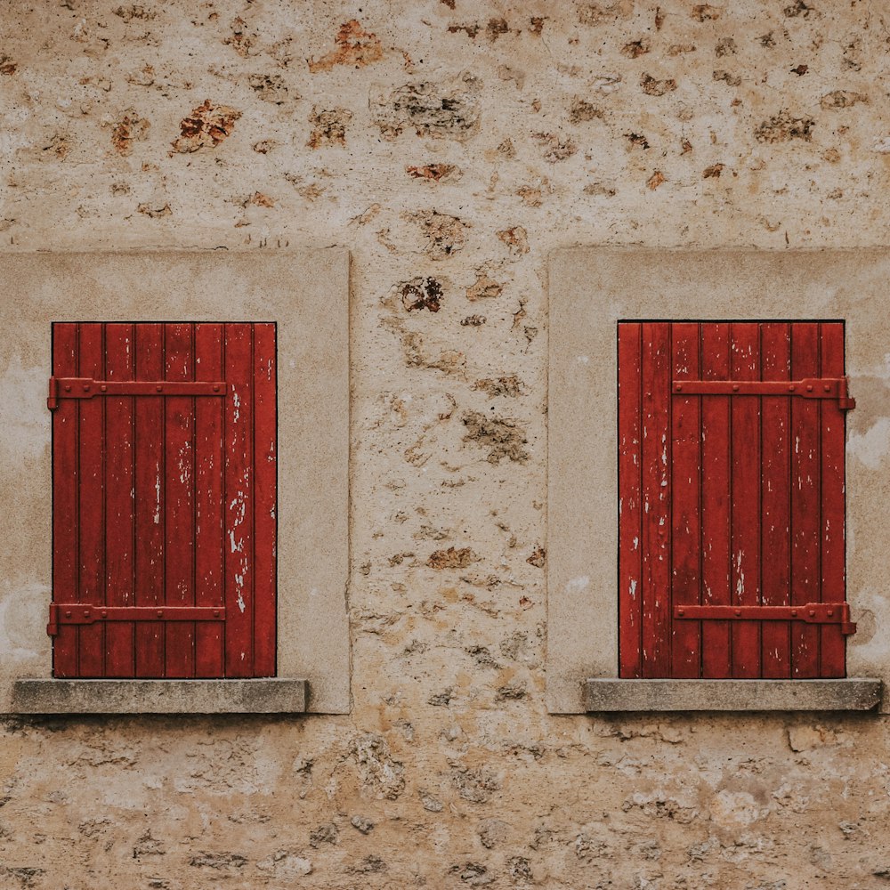 two windows with red shutters on a stone wall