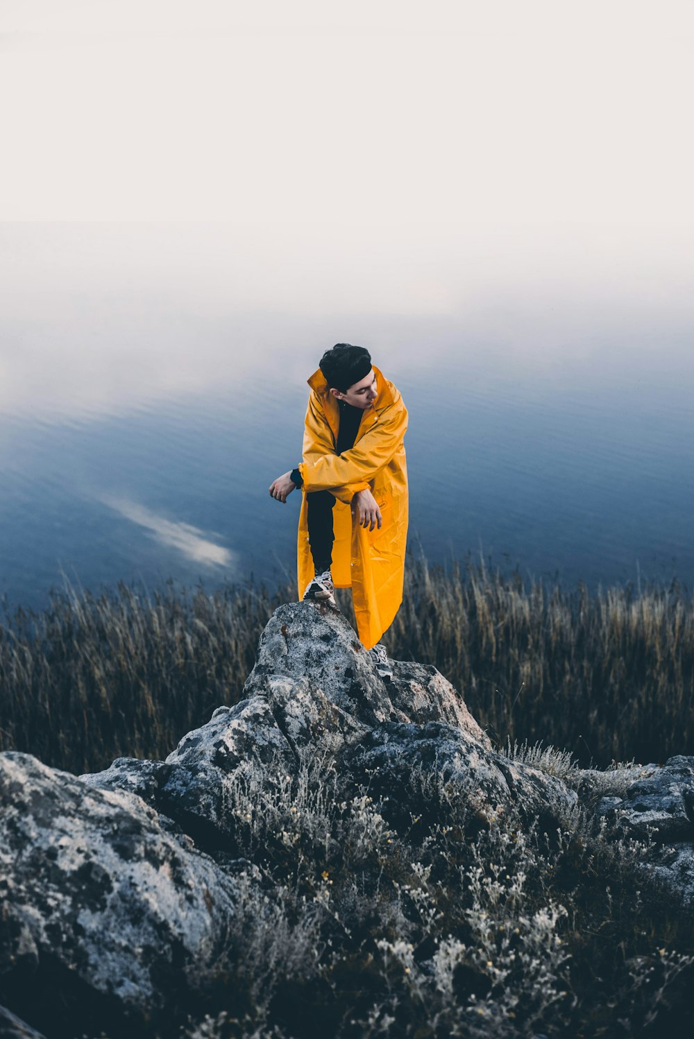 man wearing yellow coat standing on grey rocks