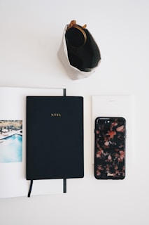 A flat lay of a handbag with accessories, including sunglasses and a notebook.