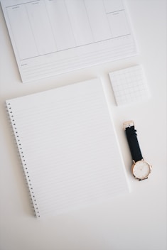 round analog watch with black leather strap on top of white wooden surface