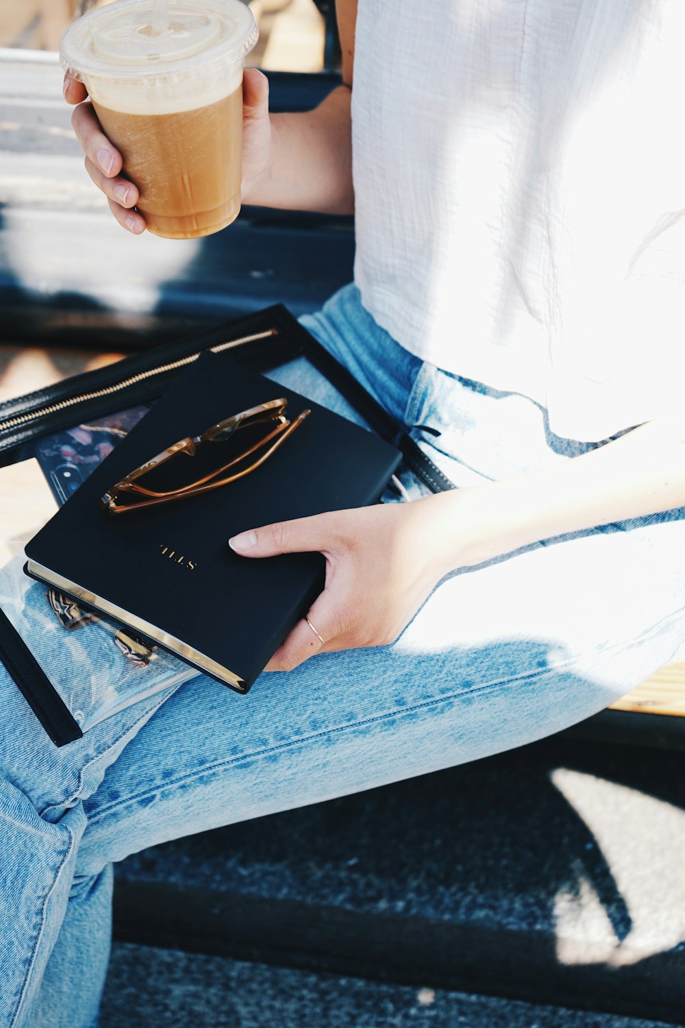 Person mit schwarzem Buch und durchsichtigem Einwegbecher aus Kunststoff