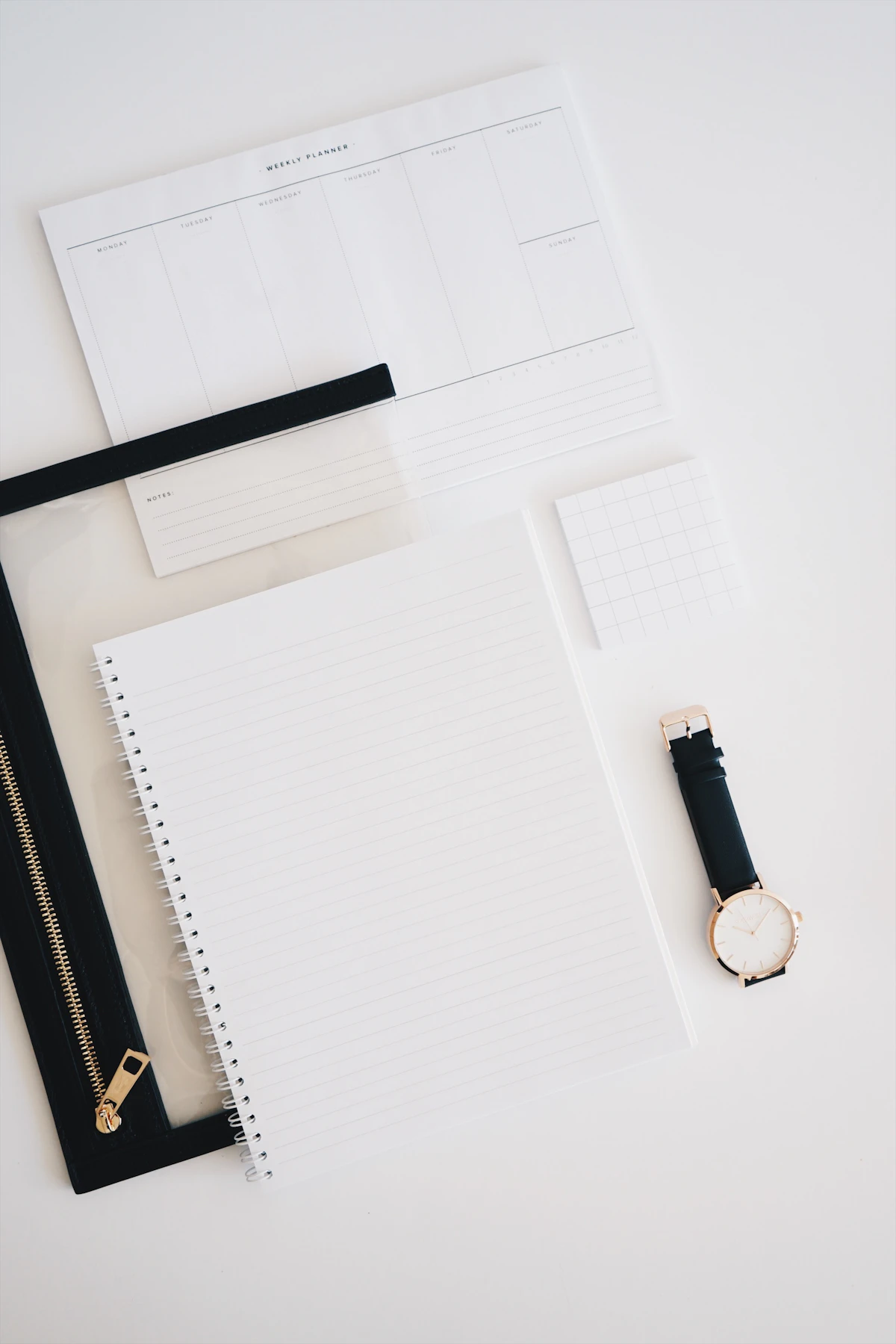 A weekly planner, a lined notebook and a watch laid out on a white surface