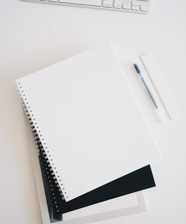 empty spiral notebook near keyboard and pen