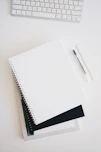 empty spiral notebook near keyboard and pen