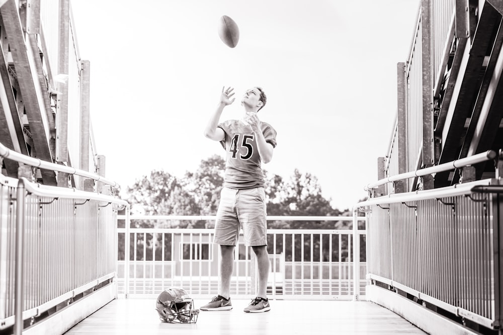 grayscale photo of man standing while tossing football outdoors