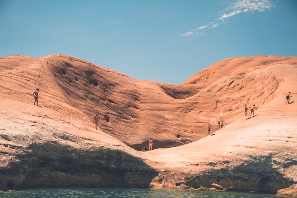 people standing on brown hill near body of water under clear blue sky