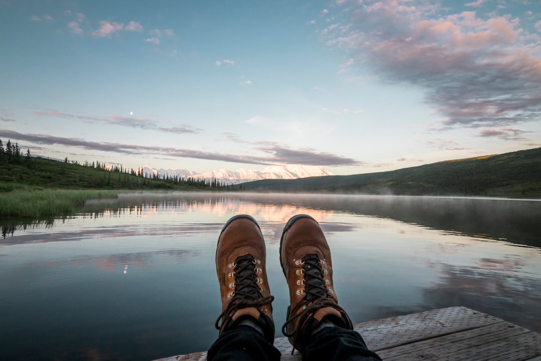 person resting foot on brown wooden platform near body of water