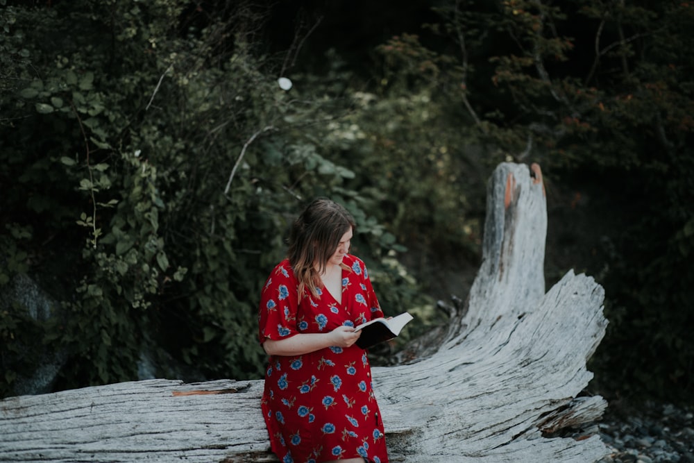 woman reading book sitting on tree log