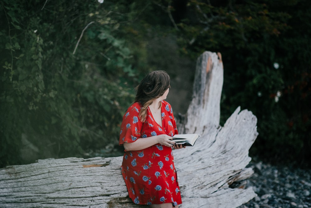 woman sitting on tree trunk while holding book