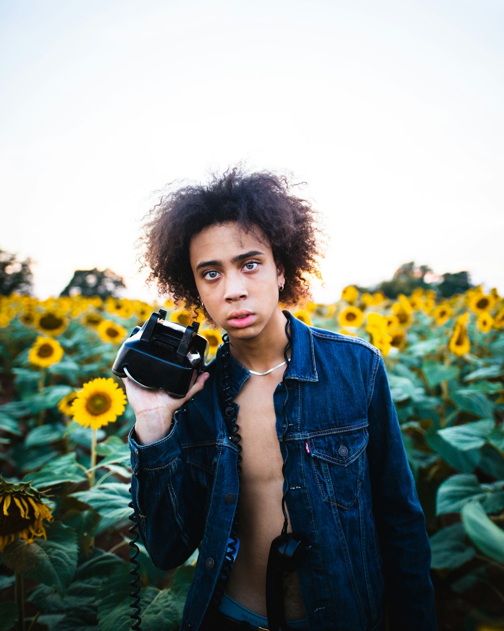 man holding black and white VR headset in front of sunflower meadow