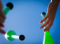Close-up of hands skillfully juggling colorful clubs under bright sunlight.