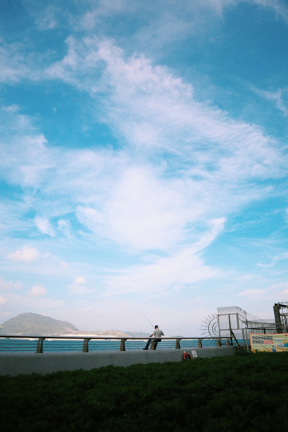 man sitting on handrail front of calm water at daytime