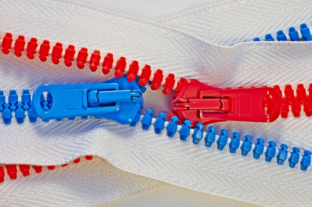 Detail of two intertwined zippers, with blue and red teeth, like male and female, on white background