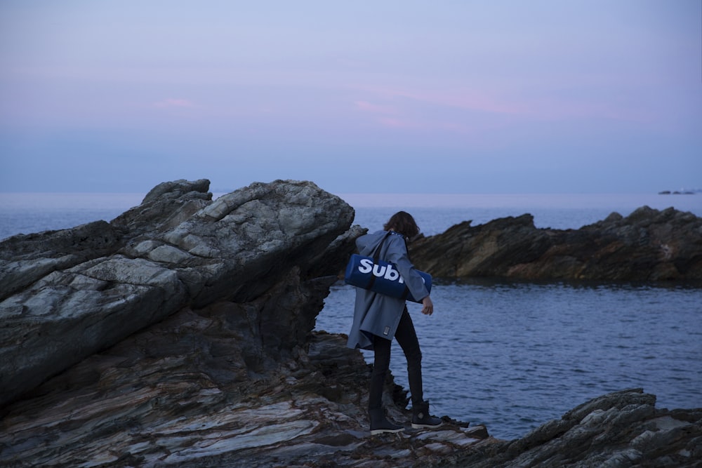 person carrying bag standing on rock