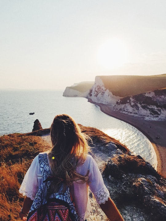 woman walking on top of mountain while looking at the seat in Durdle Door United Kingdom