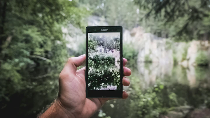 Person using a smartphone beside a bright blue lake